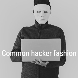 A man in a zip-up flannel jacket holding a laptop awkwardly, wearing a mask and hat. Text over the photo reads, “Common hacker fashion”